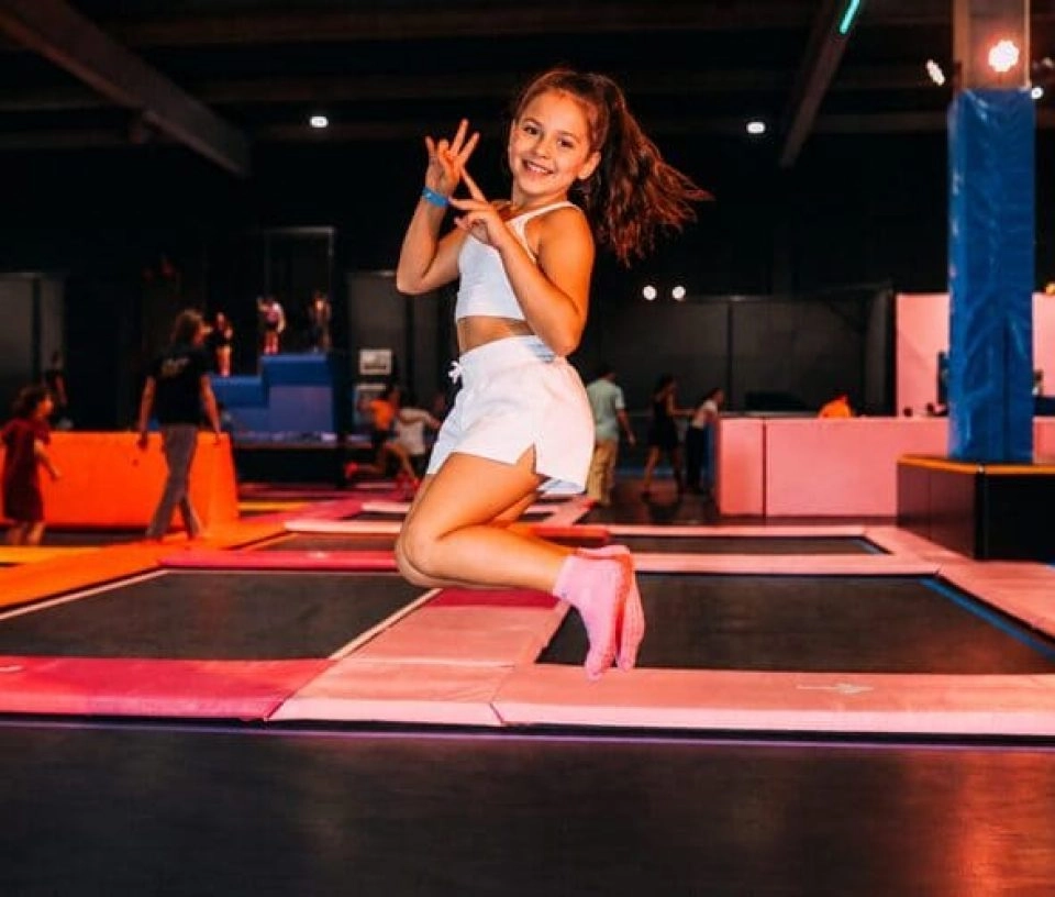 un fille pose avec le sourire devant les trampolines dans un park indoor
