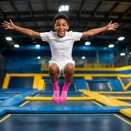 un petit garçon saute dans les airs et fait une grimace en écartant les bras sur un trampoline park you jump
