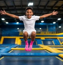 un petit garçon saute dans les airs et fait une grimace en écartant les bras sur un trampoline park you jump