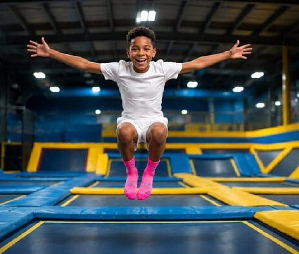 un petit garçon saute dans les airs et fait une grimace en écartant les bras sur un trampoline park you jump